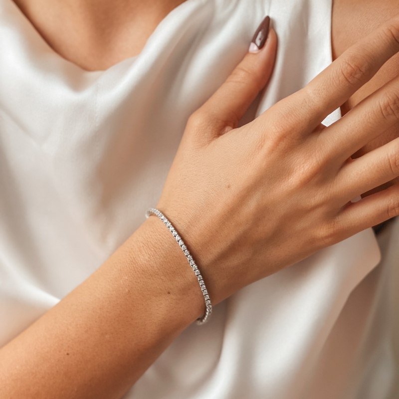 Nahaufnahme eines Handgelenks mit einem silbernen Tennisarmband, besetzt mit Zirkonia-Steinen, vor weißem Satin.