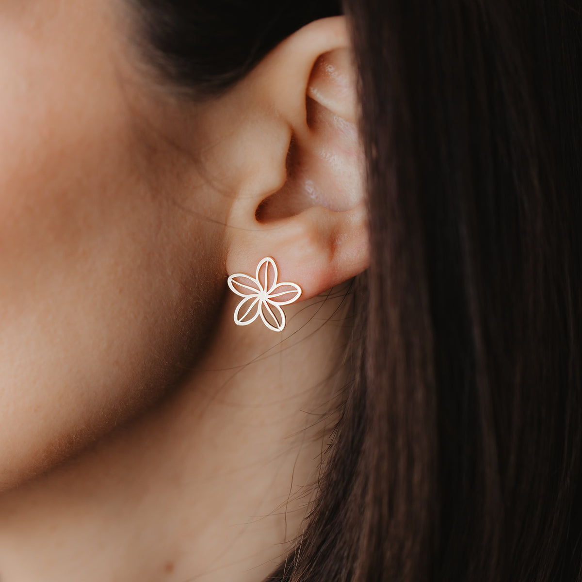 Nahaufnahme eines Ohrs, das einen filigranen Blumen-Ohrstecker aus durchbrochenem 14K Gelbgold trägt.