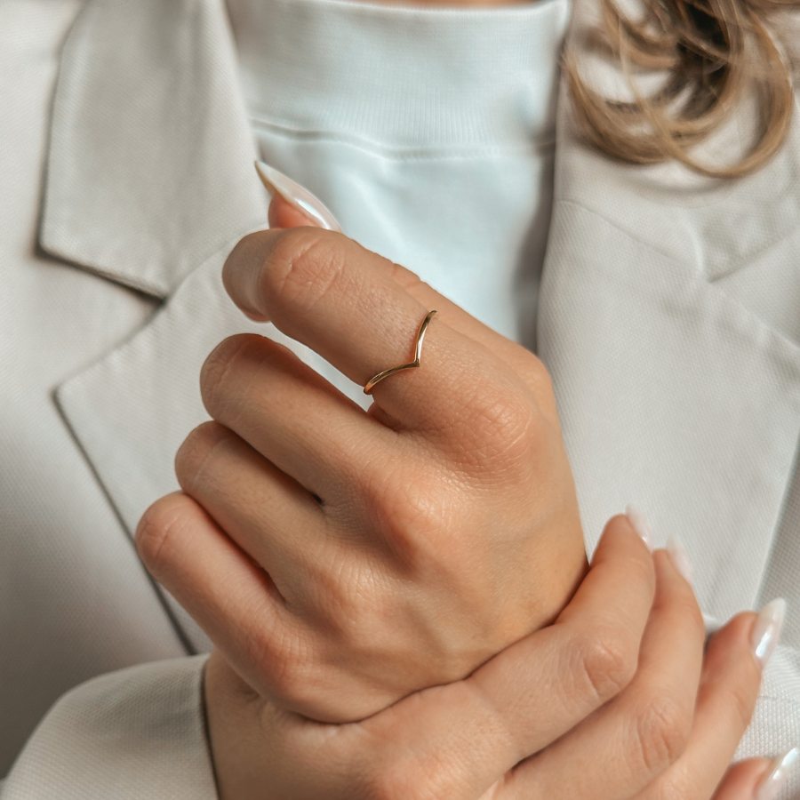 Schlichter, V-förmiger Goldring am Finger einer Person im hellen Anzug.