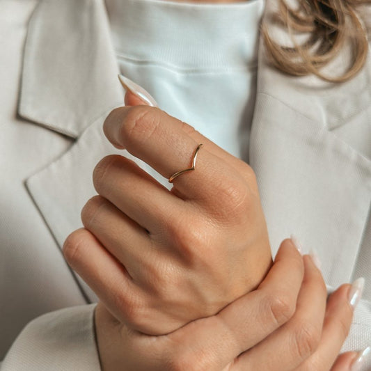 Schlichter, V-förmiger Goldring am Finger einer Person im hellen Anzug.