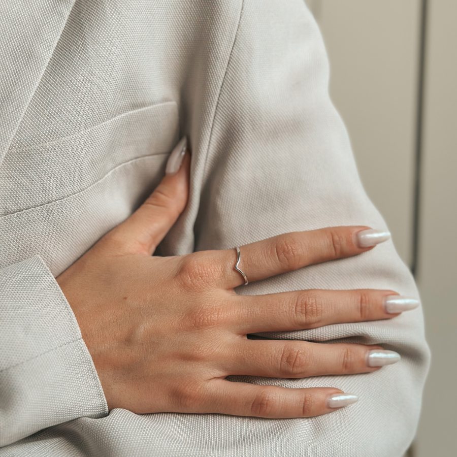 Nahaufnahme einer Hand, die einen Simple V Silver Ring vor einem neutralen Stoffhintergrund trägt.