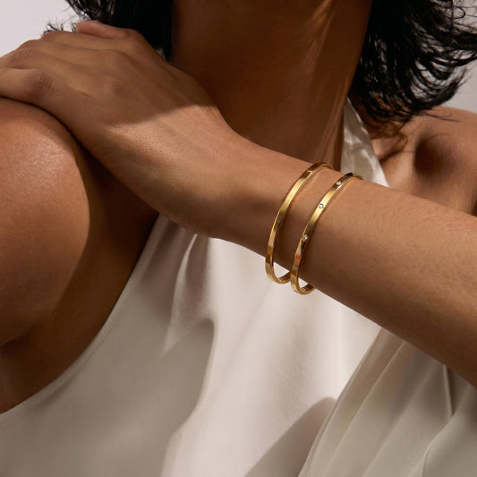 Nahaufnahme des Arms einer Person mit zwei goldenen Armreifen vor weißem Hintergrund.