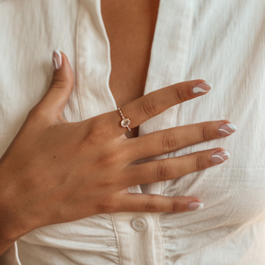 Nahaufnahme einer Frauenhand mit einem eleganten Roségold-Ring mit Mondstein; manikürte Nägel, weiße Bluse.