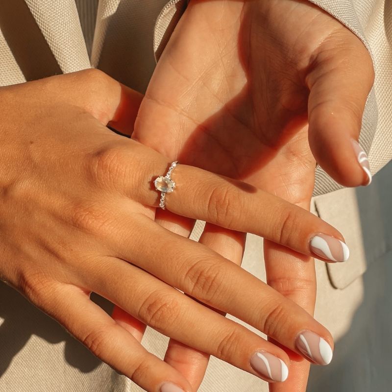 Hände zeigen den Selah Silver Ring mit Mondstein vor einem weichen Hintergrund.