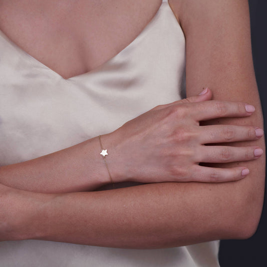 Arm einer Frau mit einem zarten 14K-Gold-Sternarmband vor einem hellen Satintop.