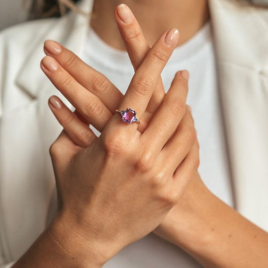 Gekreuzte Hände zeigen einen Silberring mit Amethyst- und Tansanitsteinen.