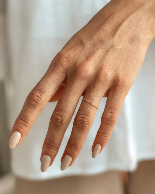 Eine zarte Hand mit nudefarbenen, manikürten Nägeln trägt einen 14K-Gold-Kettenring.