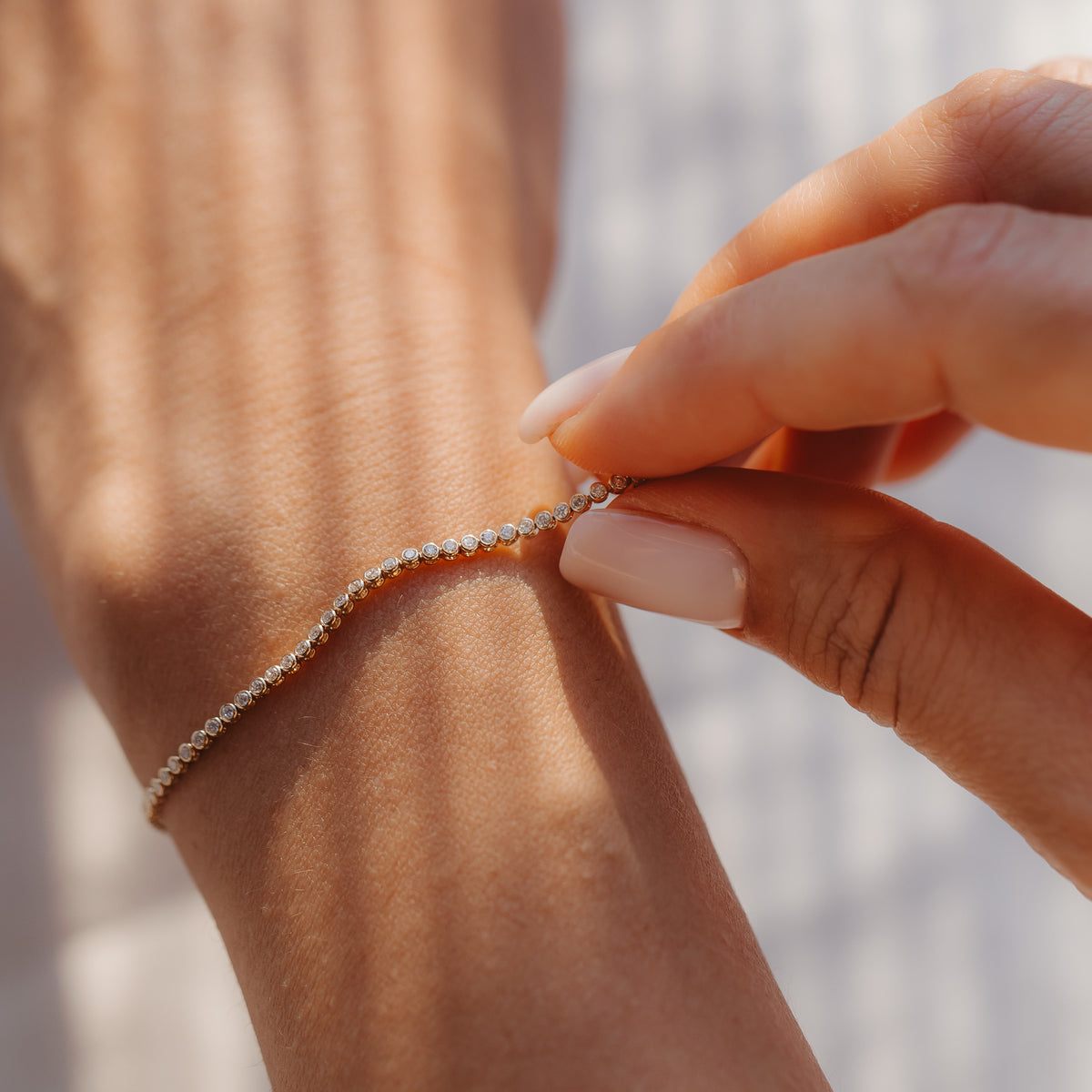 Nahaufnahme einer Hand, die ein Diamant-Tennisarmband aus 14K Gelbgold am Handgelenk schließt, im sanften Sonnenlicht.