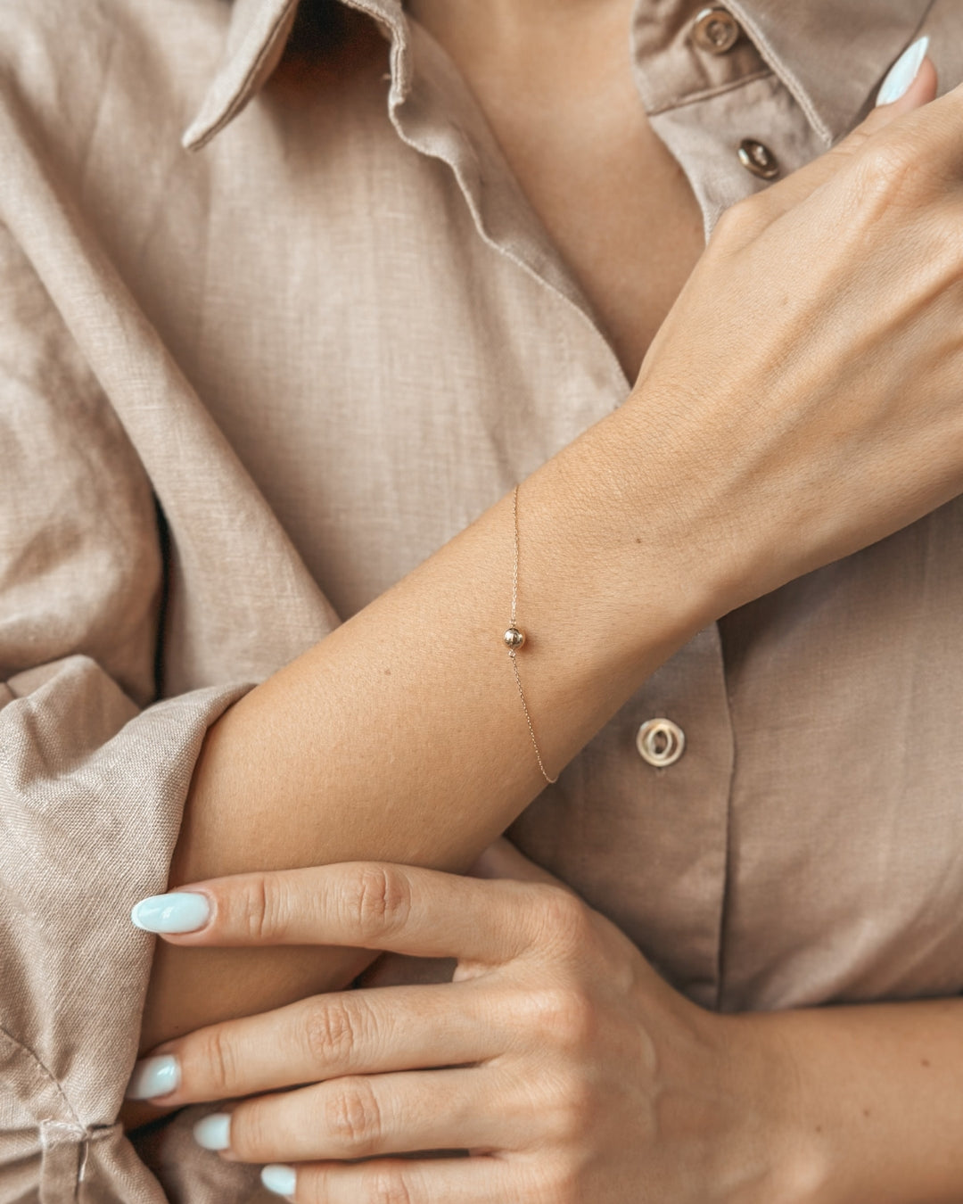 Nahaufnahme einer Person mit einem zarten Goldarmband am Handgelenk; ein beigefarbener Hemdsärmel betont die elegante Ausstrahlung des Accessoires.