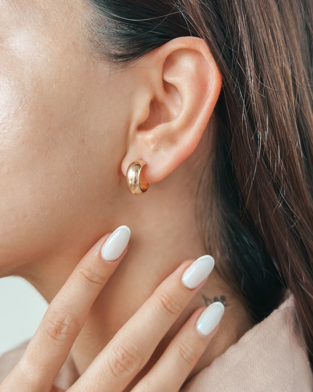 Nahaufnahme eines Frauenohrs mit einem goldenen Creolen-Ohrring, wobei manikürte Finger ihren Hals berühren.