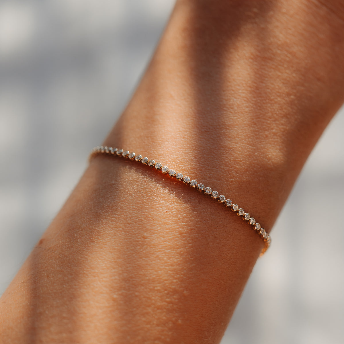 Nahaufnahme eines zarten 14K Gelbgold-Tennisarmbands mit kleinen runden Diamanten, am Handgelenk getragen und von weichem natürlichen Licht beleuchtet.