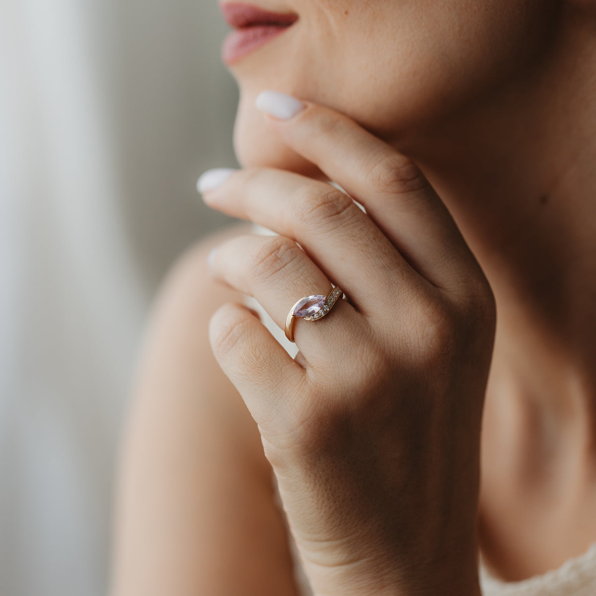 Nahaufnahme einer Hand nah am Gesicht, die den Velvet Rose Ring aus 14K Gelbgold mit einem rosafarbenen Saphir im Marquise-Schliff und kleinen Akzentdiamanten trägt.