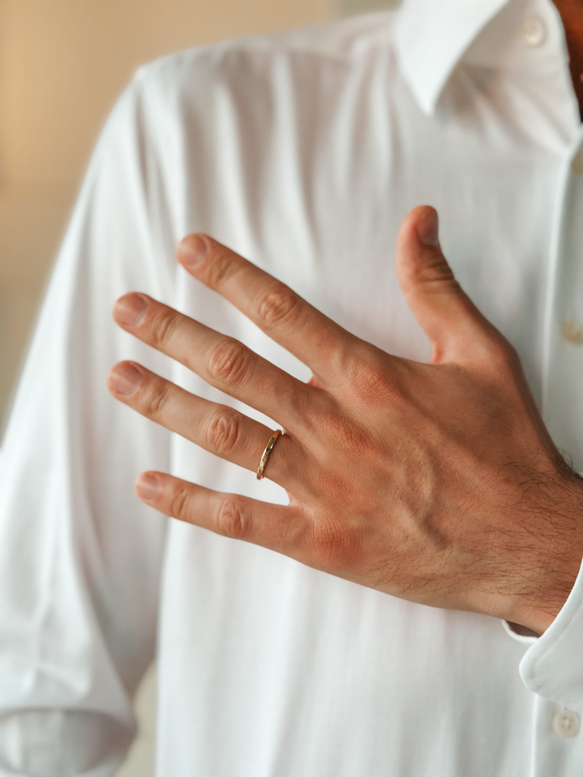 Eine Hand mit goldenem Ehering am Ringfinger, die auf einem weißen Hemd ruht.