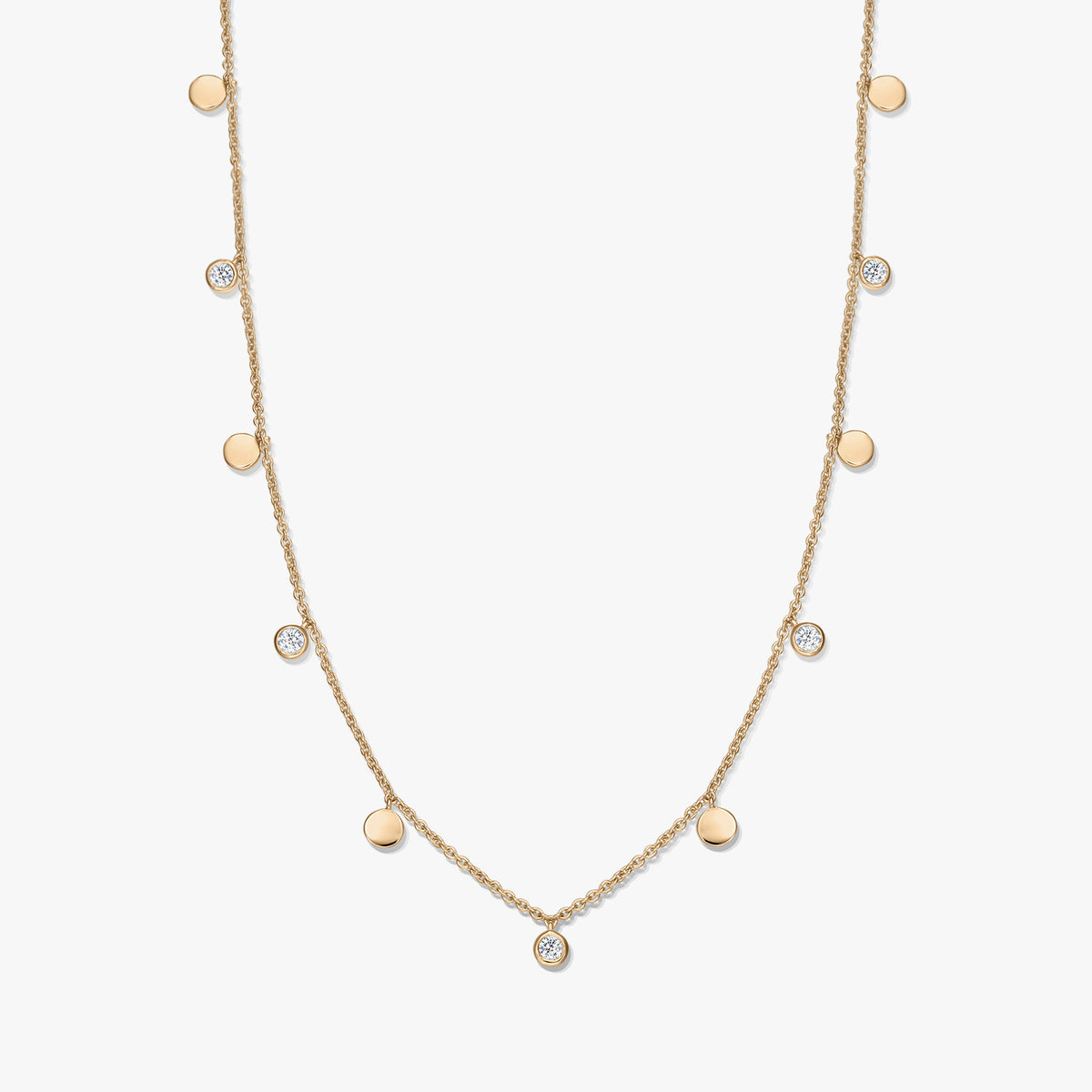 Station-Collier aus vergoldetem Sterlingsilber mit abwechselnd angeordneten kleinen polierten Scheibenanhängern und weißem Topas in Zargenfassung an einer zarten Kette, vor weißem Hintergrund fotografiert.