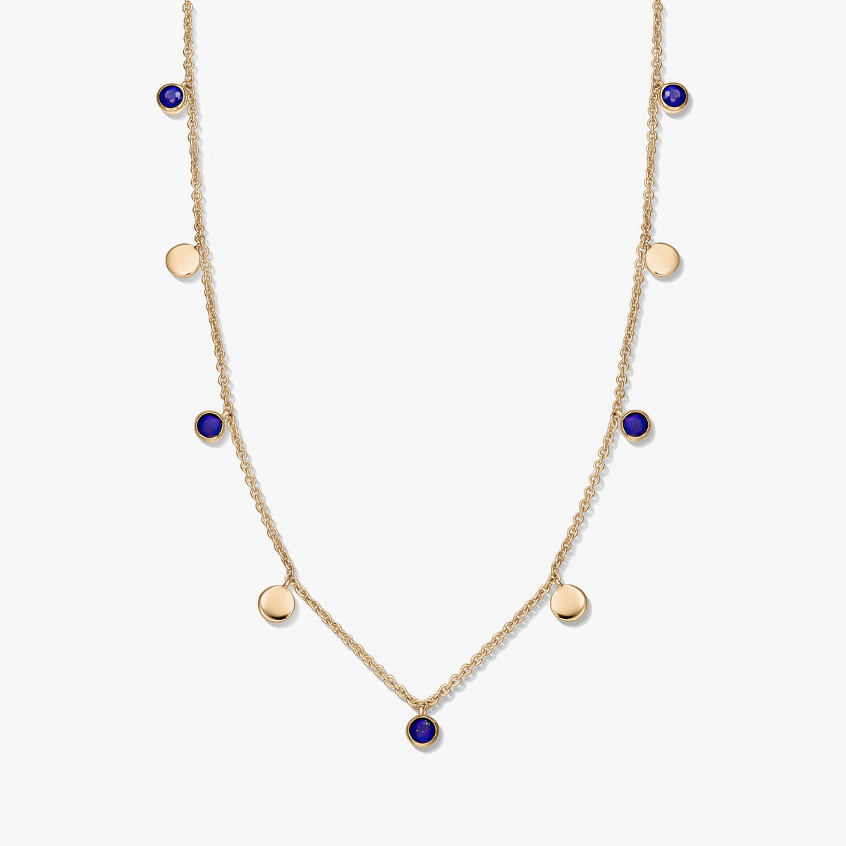 Zarte Stationkette aus vergoldetem Sterlingsilber mit runden Lapislazuli-Cabochons und kleinen goldenen Scheibenanhängern, vor weißem Hintergrund fotografiert.