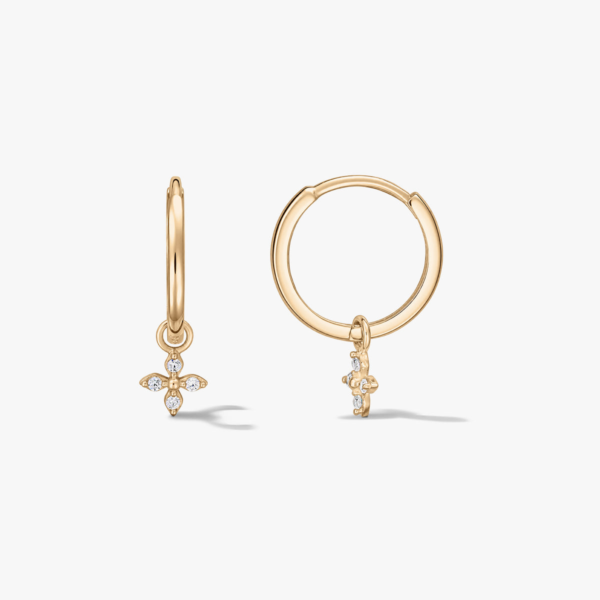 Paar Creolen aus 14K Gelbgold mit kleinen, mit Zirkonia besetzten, vierblättrigen Blütenanhängern auf weißem Hintergrund.