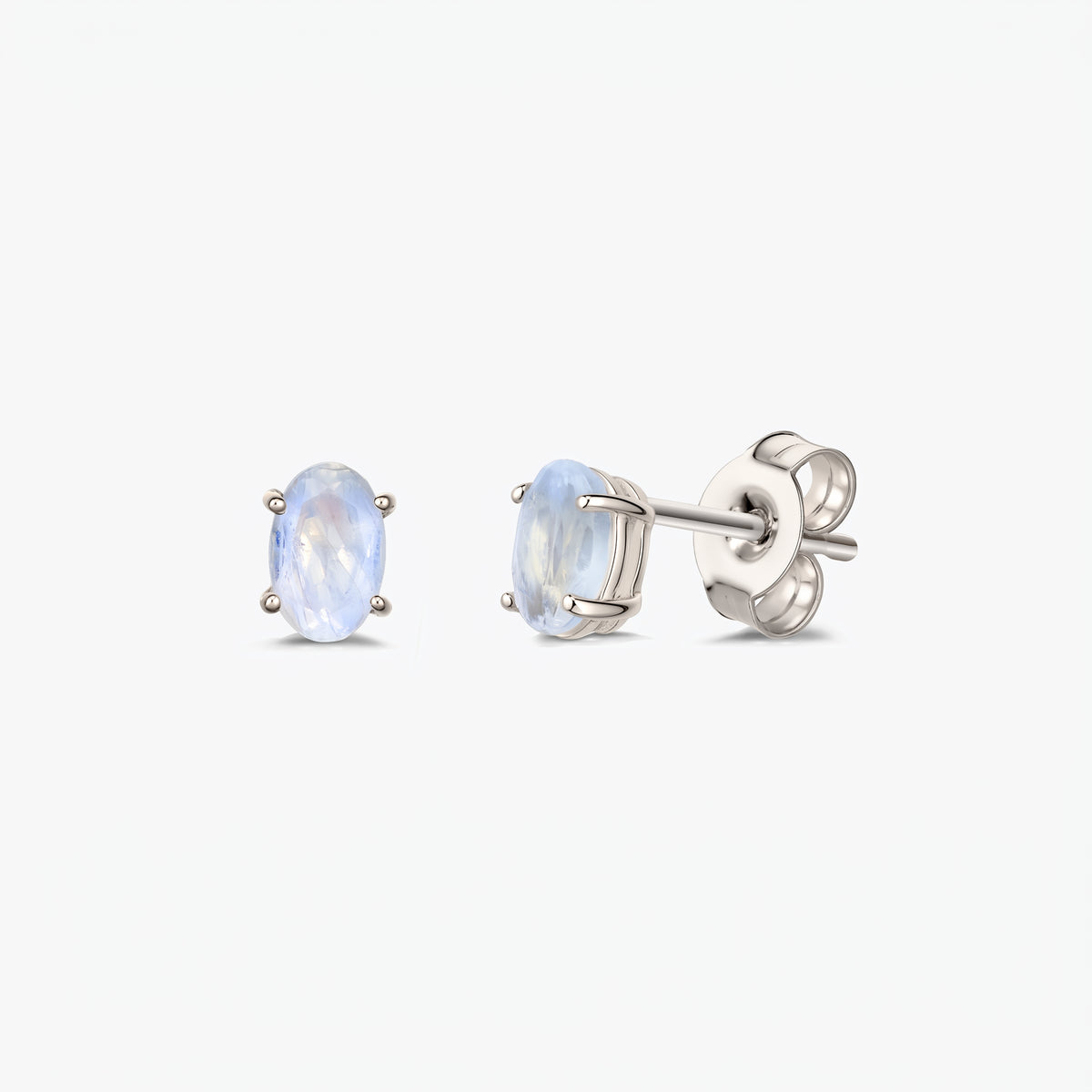Pair of silver moonstone stud earrings with oval faceted stones in four‑prong settings and butterfly push backs, shown on a white background.