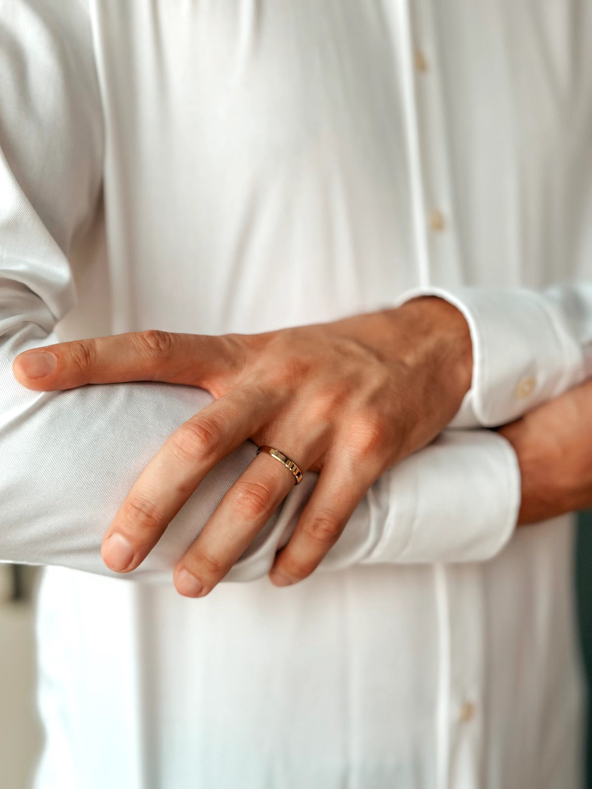 Nahaufnahme einer Person in weißem Hemd, die einen goldenen Ehering an der Hand zeigt.