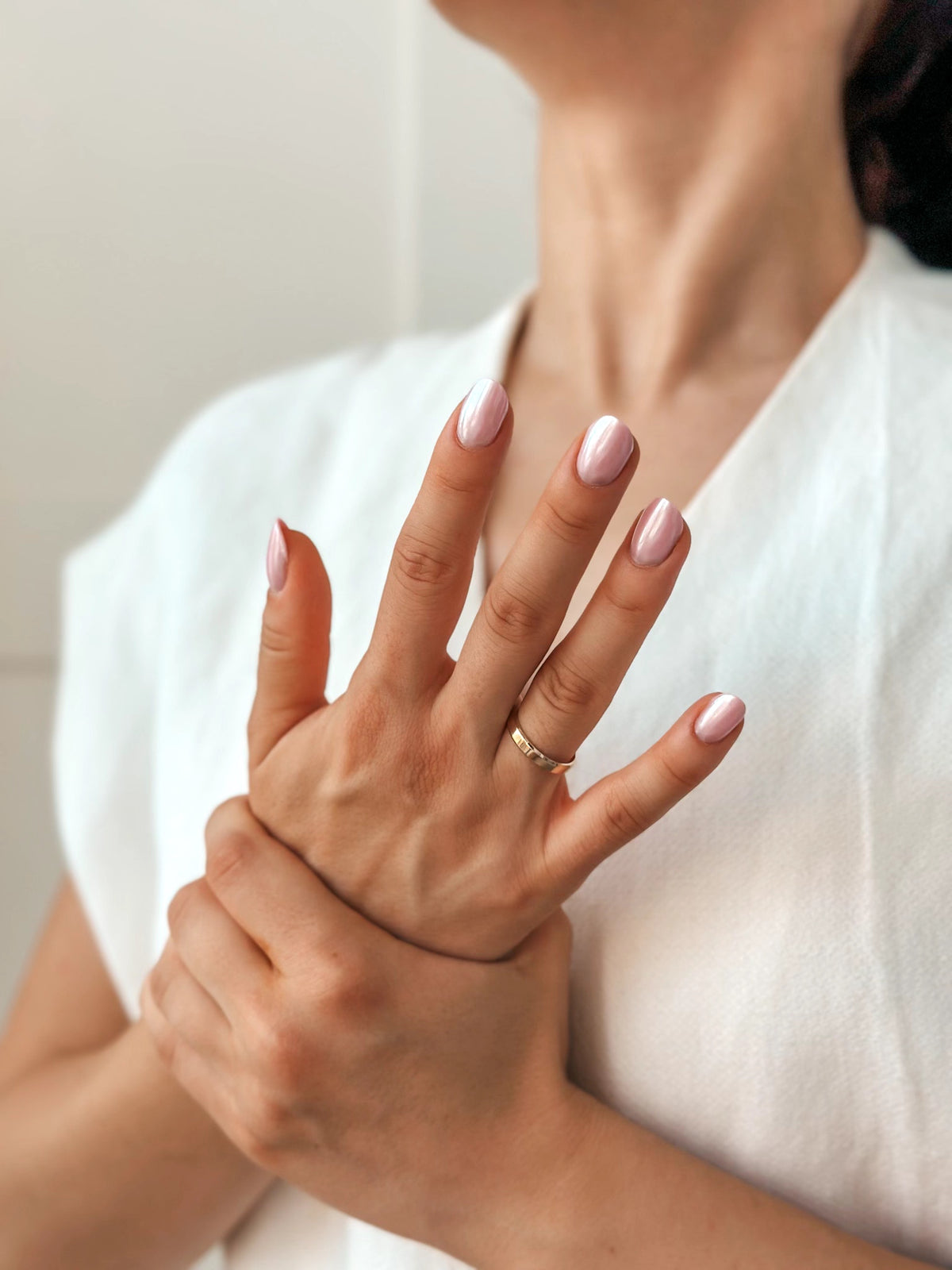 Nahaufnahme von Händen einer Frau mit rosa Nagellack, die einen goldenen Ehering trägt, vor hellem Hintergrund.