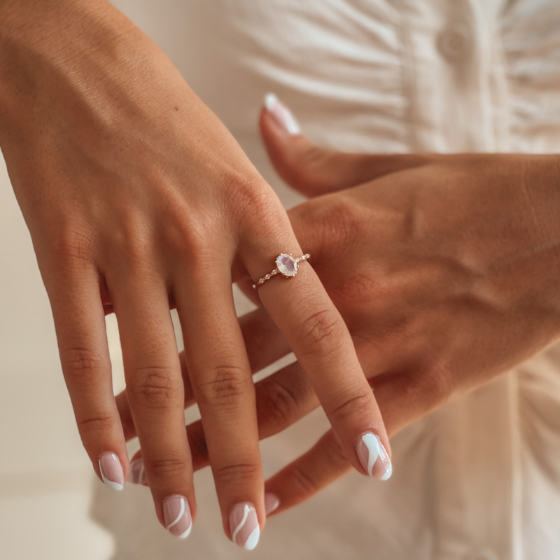 Nahaufnahme von Händen mit Nageldesign, die einen Mondsteinring aus Roségold tragen.